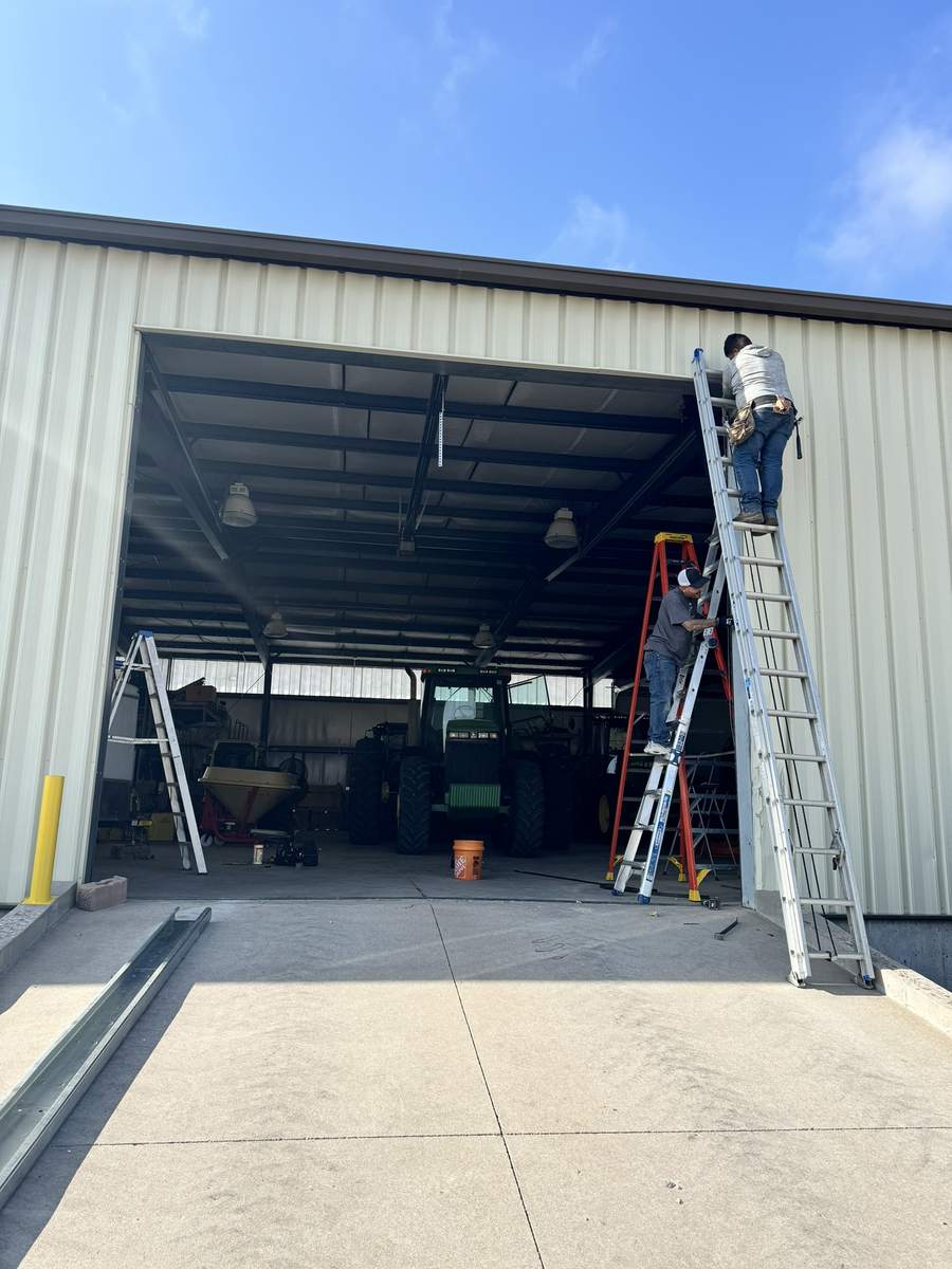 Exteriors Denver technicians on ladders at a large steel-building door