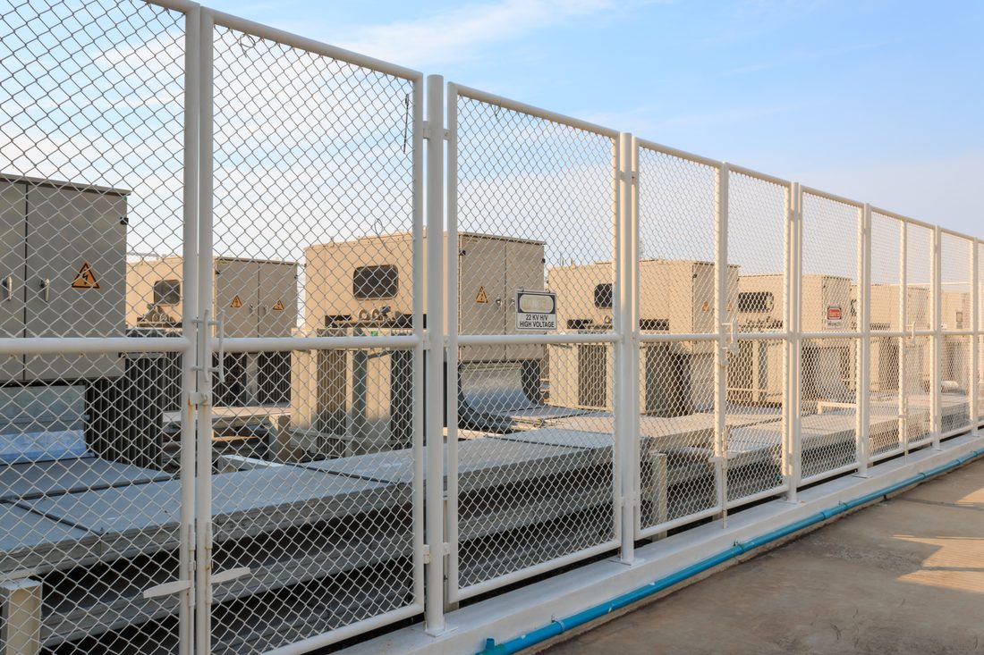 White chain-link security fencing around rooftop electrical equipment